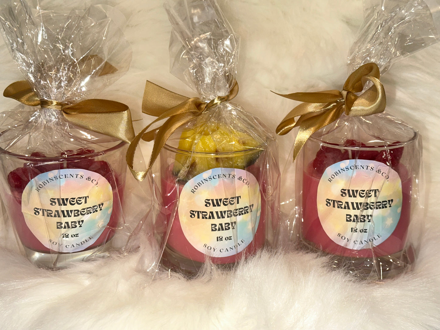 Three sweet strawberry baby candles in clear packaging with gold ribbons on a white background.