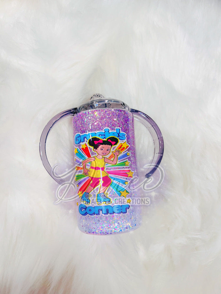 A multicolored sippy cup with glitter and a design of a character on the side, set against a white furry background.