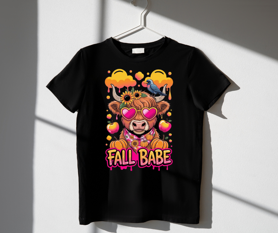 Black t-shirt with a colorful graphic design featuring a cow, pumpkins, and the text 'Fall Babe' on a white background.