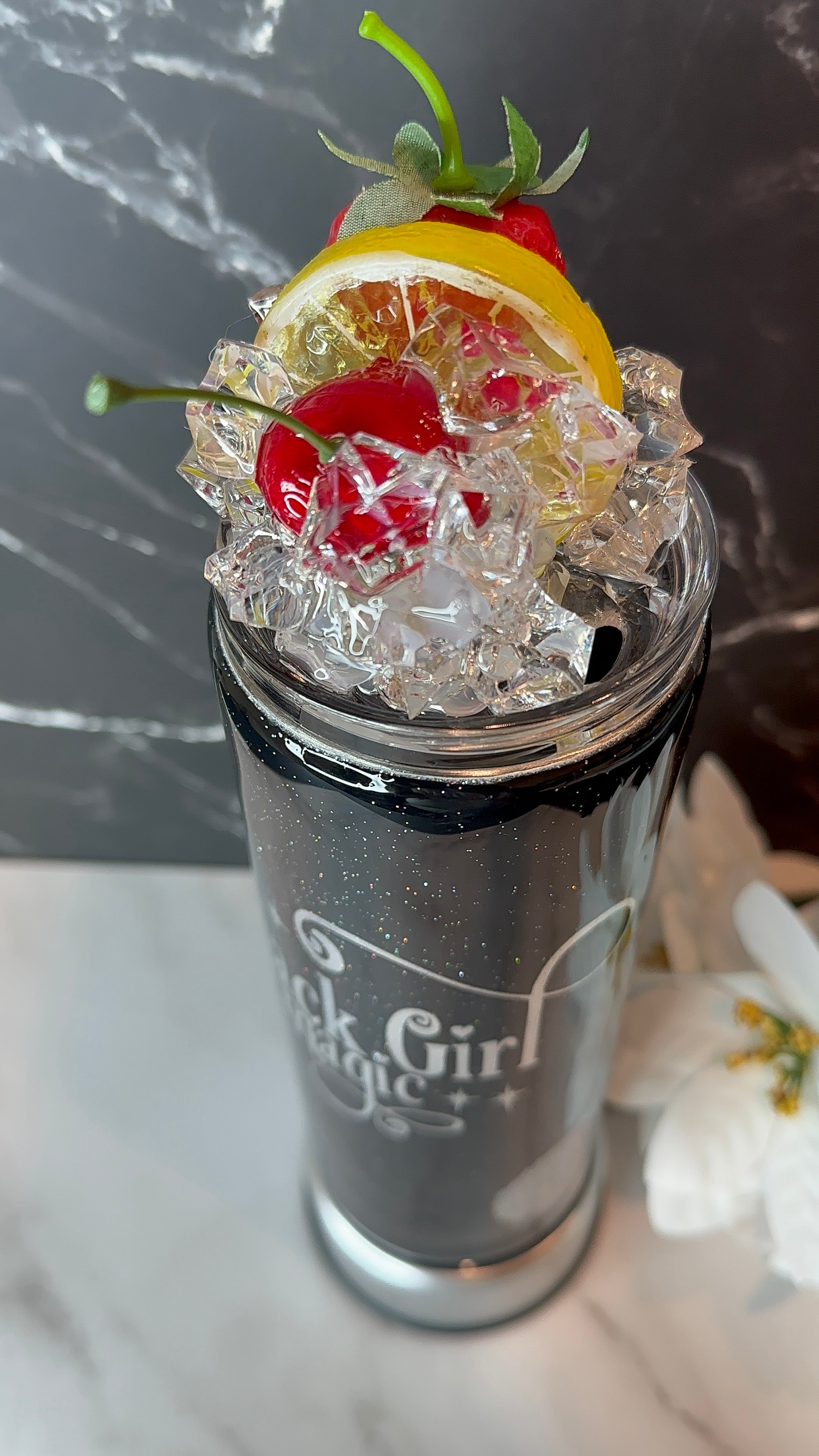 Tumbler with ice, lemon, cherry, and green leaf on a marble surface