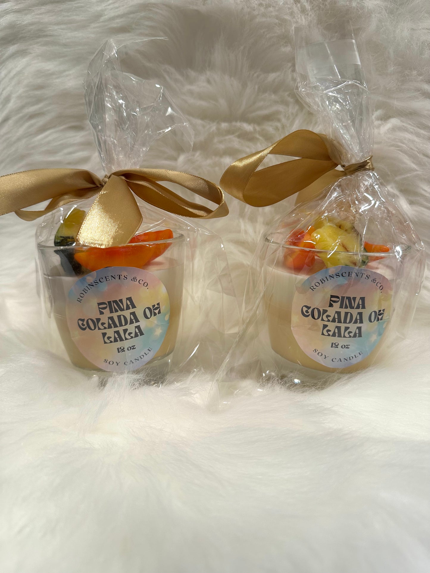 Two small candles with scented fruit embeds and gold ribbons on a white fluffy surface