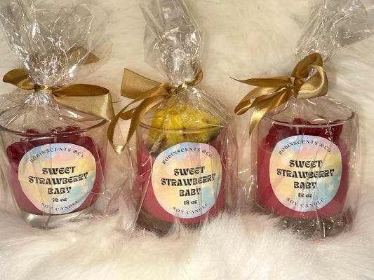 Three sweet strawberry baby candles in clear packaging with gold ribbons on a white background.